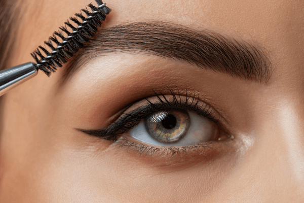 Un pinceau applique de l'huile de ricin sur un sourcil