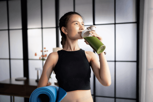 Une femme boit du matcha et tient un tapis de yoga